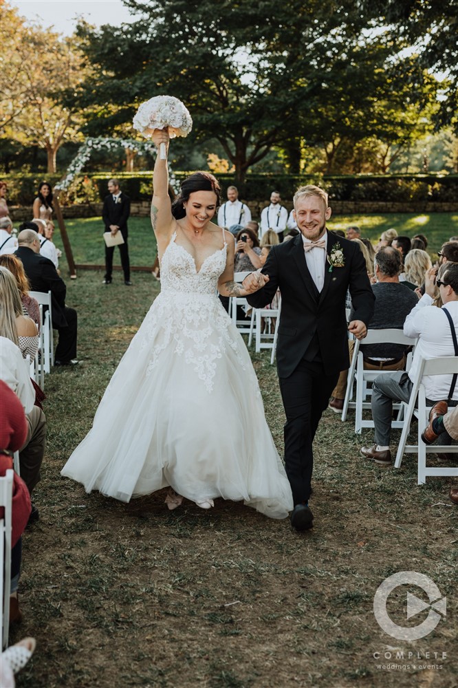 bride holds up bouquet while walking away from ceremony