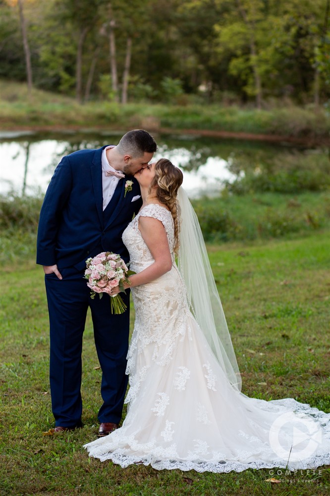 bride and groom kiss beside pond