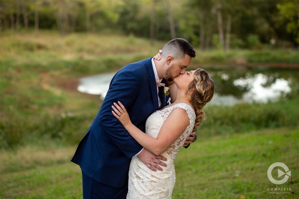 bride and groom kiss in front of pond
