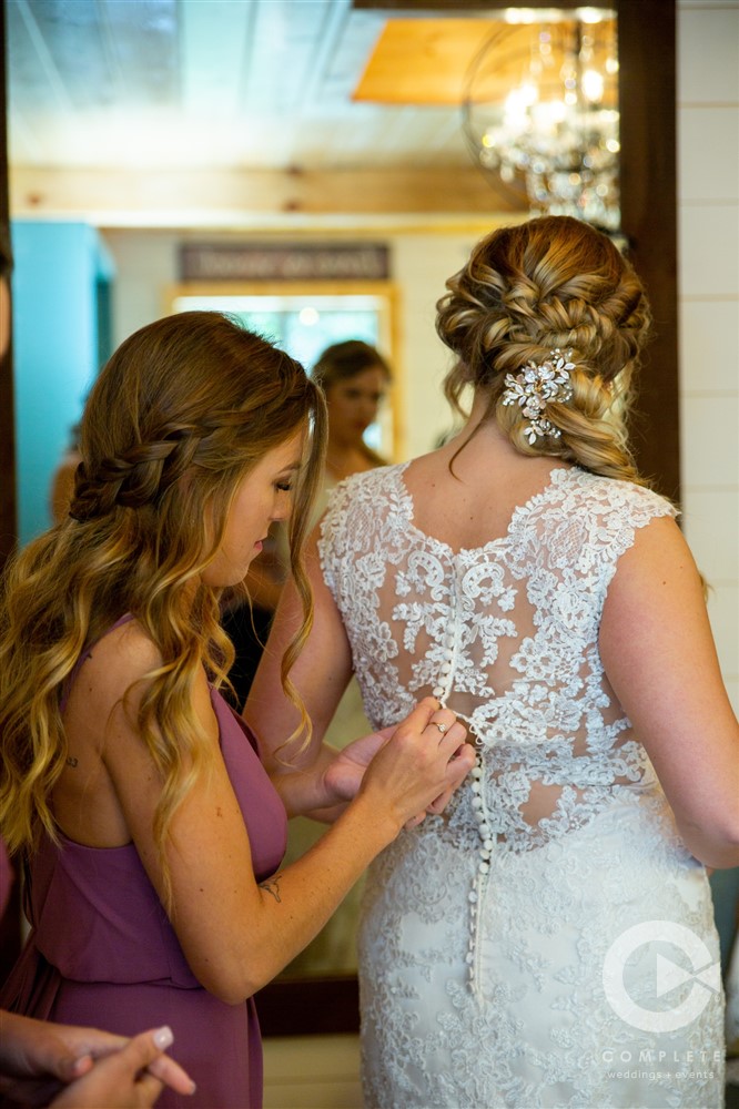 bride being buttoned up before ceremony