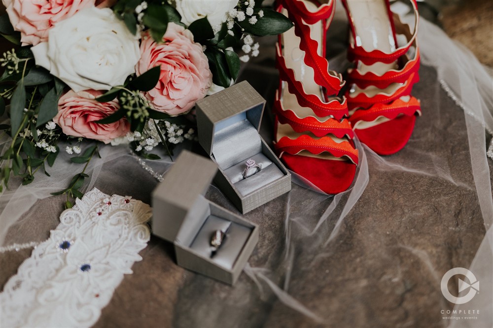 focus shot of red shoes, rings, garter, and bouquet