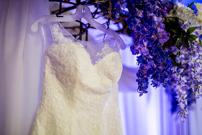 wedding dress hanging on arbor with purple flowers