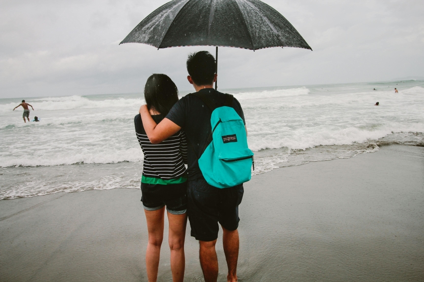 Couple on beach with umbrella during rain