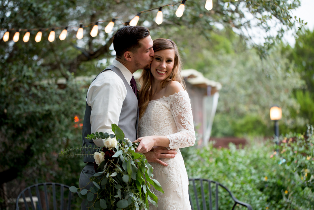 groom kiss bride greenery